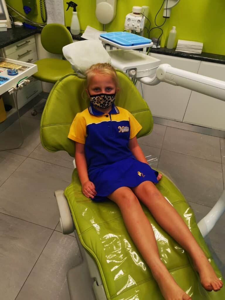 Kid in dental chair with mask, hospital dental care, young girl dental patient at clinic.